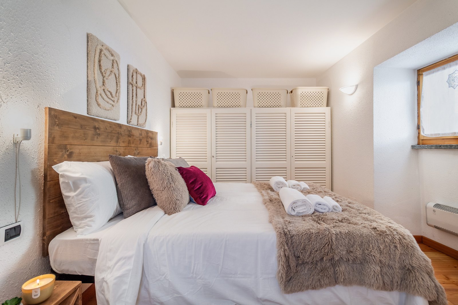 10_relooking-appartamento-montagna-camera-da-letto-matrimoniale-moderno-design-accogliente-elegante.jpg Camera da letto moderna con testiera in legno, biancheria bianca, cuscini dai toni neutri e uno bordeaux; atmosfera calda e accogliente con dettagli curati e stile contemporaneo.