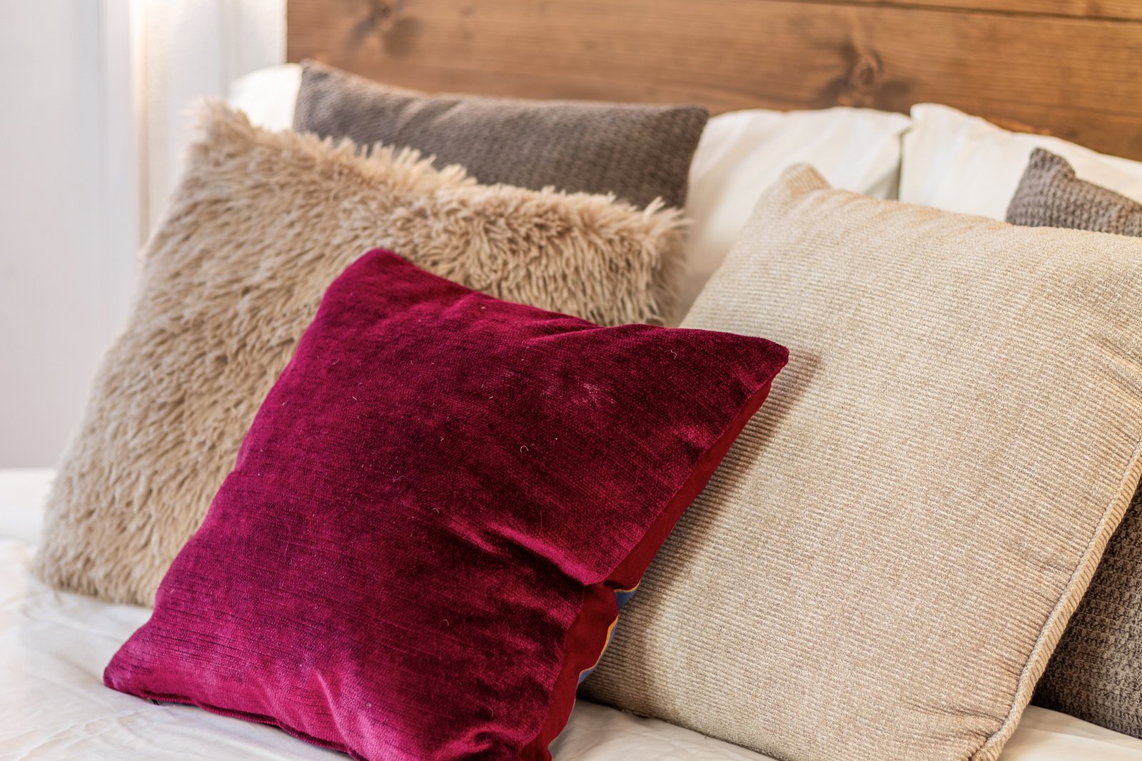 11_dettaglio-cuscini-toni-neutri-bordeaux-camera-da-letto-matrimoniale-elegante.jpg Dettaglio di cuscini su letto matrimoniale con testiera in legno, tessuti morbidi e colori caldi, atmosfera accogliente e raffinata.