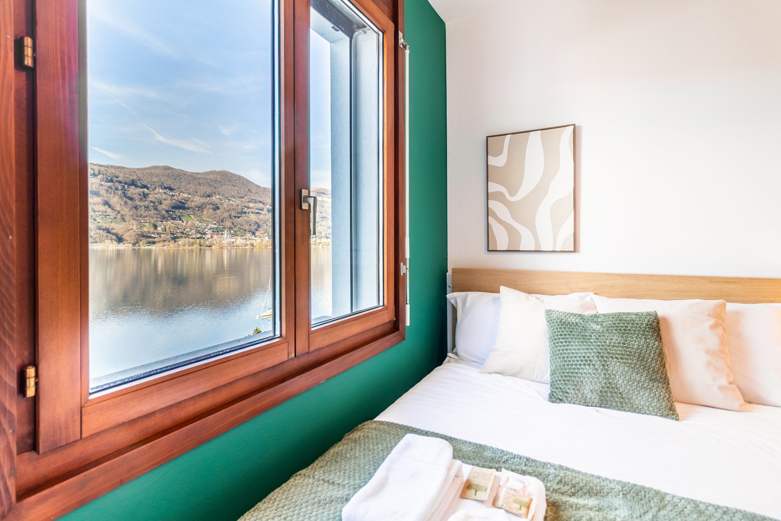 11_dettaglio-letto-camera-matrimoniale-vista-lago-finestra.jpg Dettaglio del letto con vista lago, tessili verdi e beige e design pulito.