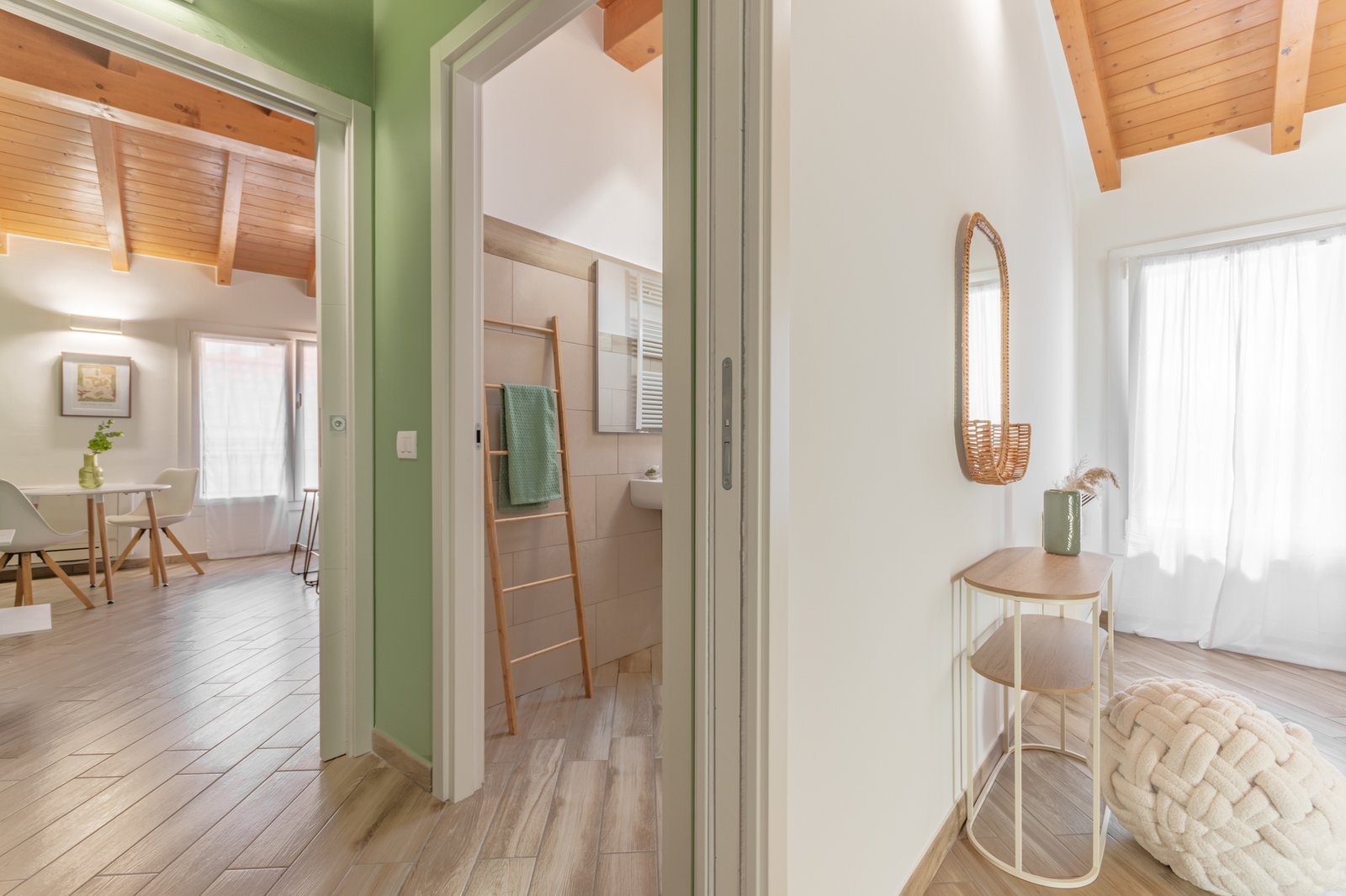 12_home-staging-collegamento-camera-bagno-cucina-disimpegno-salvia.jpg Vista di collegamento tra camera, bagno e cucina mansardati, con disimpegno color salvia come elemento di continuità. Gli ambienti, luminosi e con travi a vista, mostrano la camera elegante, il bagno raffinato e la cucina modeerna in un insieme armonioso.