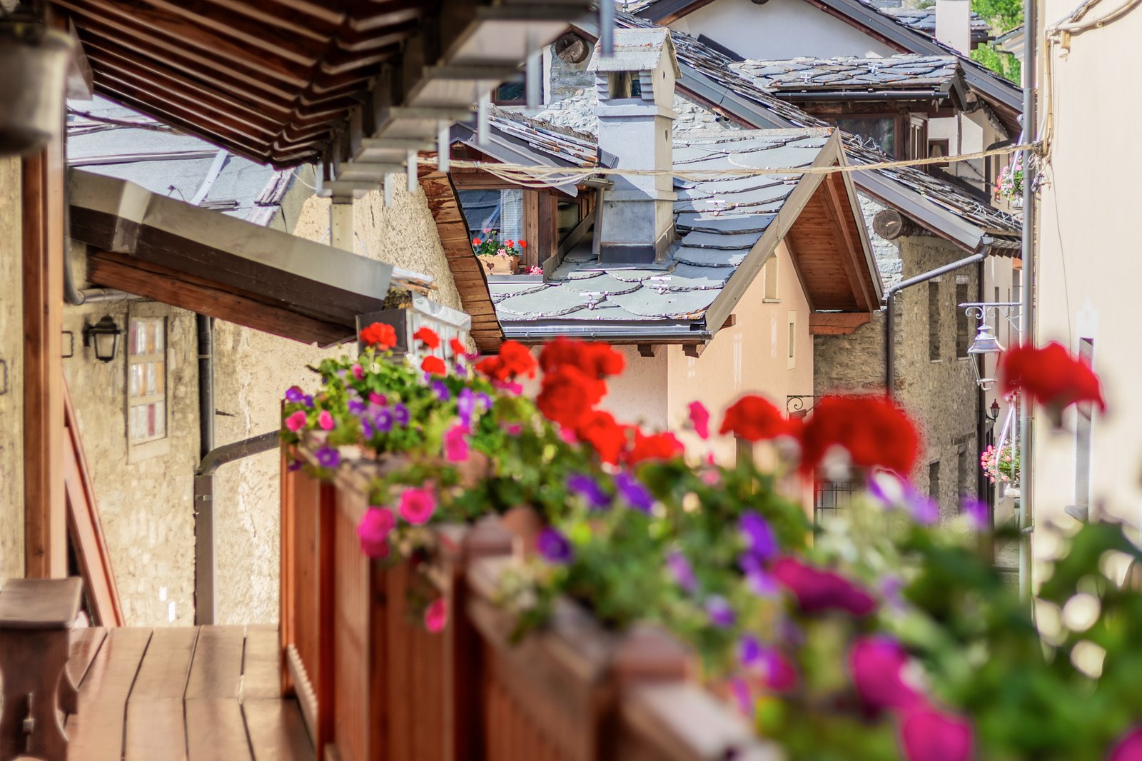 15_dettaglio-balcone_fiorito_vista_borgo_montano.jpg Balcone in legno con fiori colorati che si affaccia su un caratteristico borgo di montagna, tetti in pietra e atmosfera autentica e suggestiva.