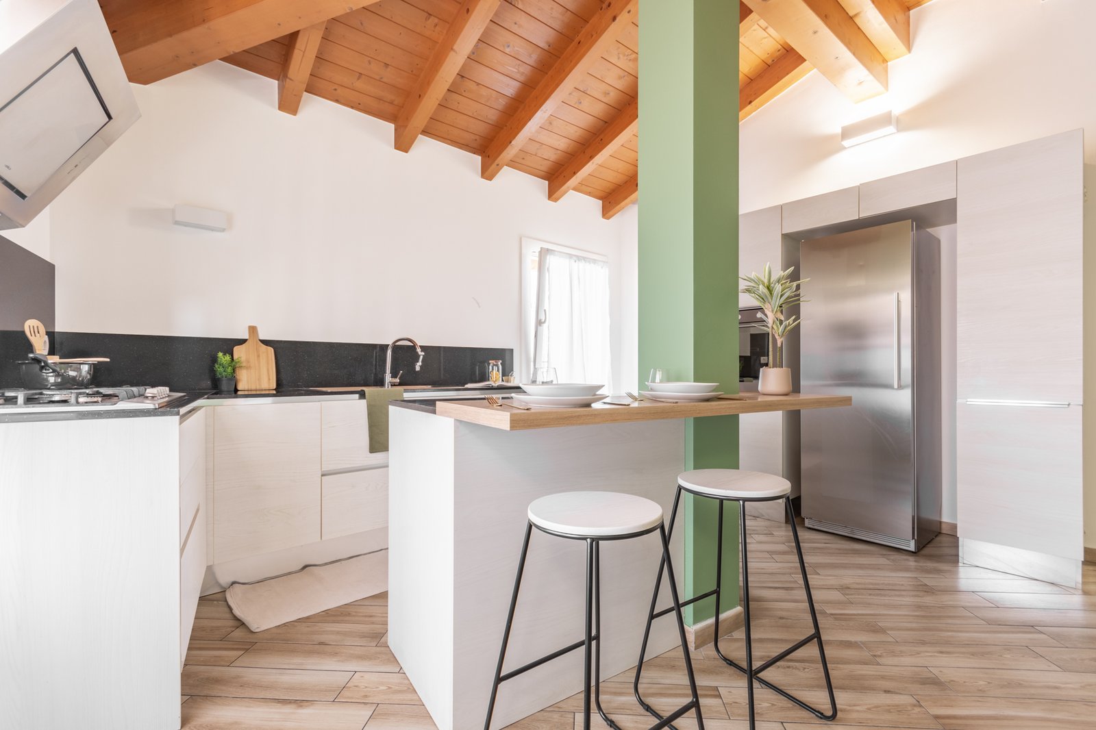 15_home-staging-cucina-moderna-mansardata-blocco-cucina-bianco-schienale-nero-isola-bianca-piano-legno.jpg Cucina mansardata luminosa con blocco cucina bianco e schienale nero di design, affiancata da un’isola centrale con struttura bianca e piano in legno color miele. L’ambiente è moderno, elegante e armonioso, valorizzato dalle travi in legno a vista.