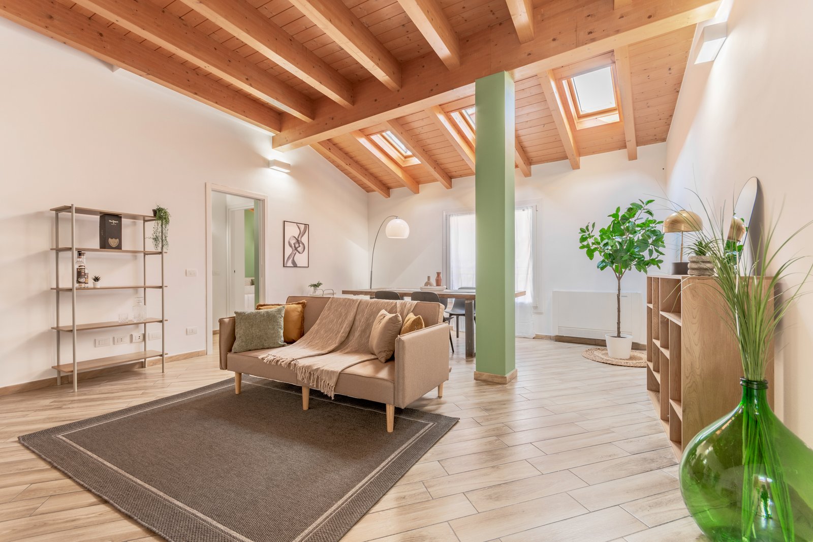 Soggiorno mansardato ampio e luminoso, con travi in legno a vista e arredi moderni ed eleganti nei toni del beige, verde salvia e senape, con atmosfera calda e raffinata.