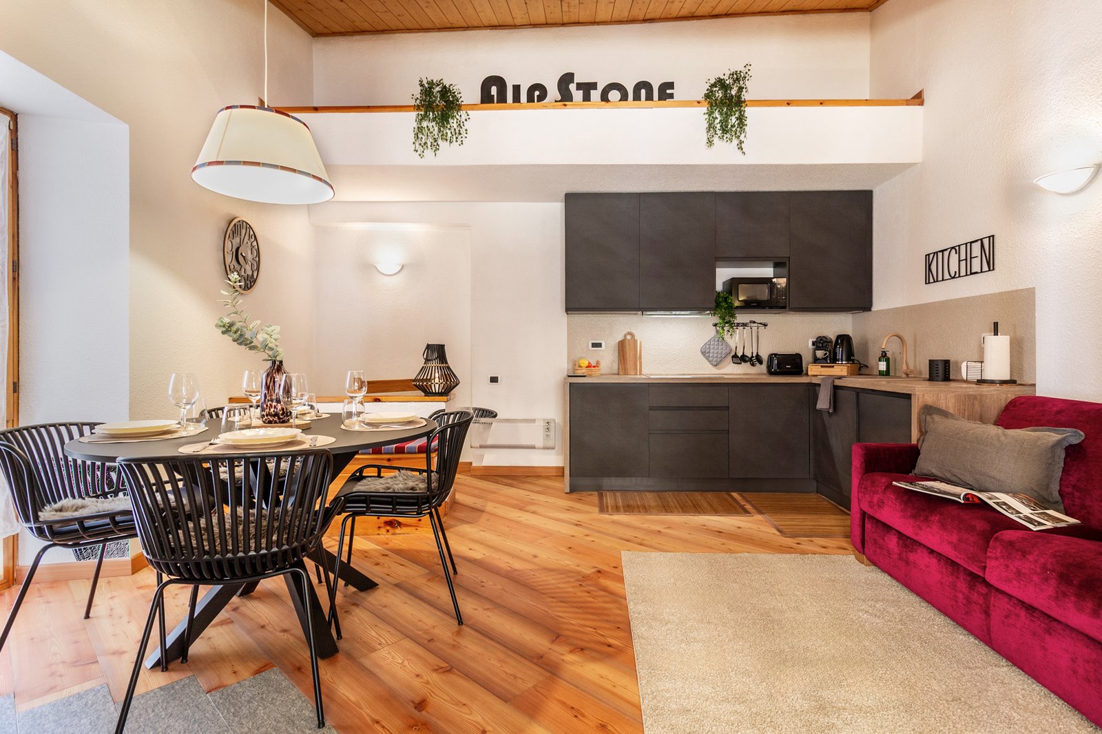 1_relooking-appartamento-montagna-moderno-open-space-legno-design.jpg Open space moderno con cucina grigio antracite, tavolo da pranzo nero e divano bordeaux; appartamento elegante e accogliente.