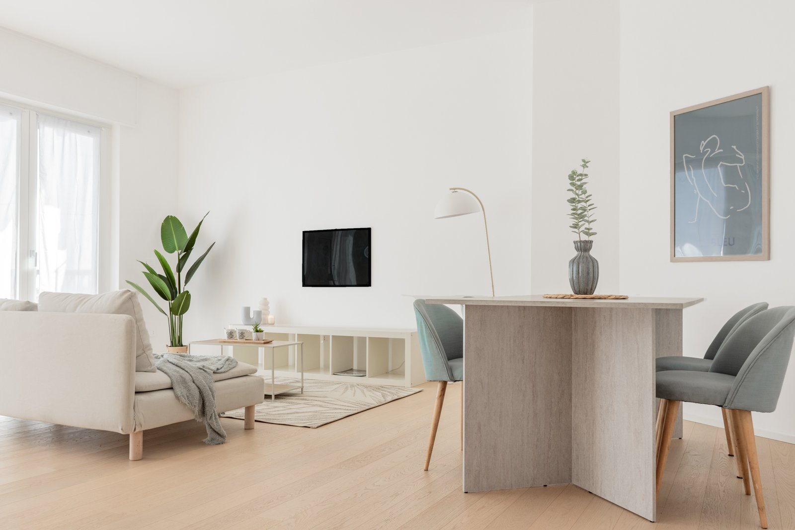 Soggiorno open space luminoso con divano bianco, tavolo effetto travertino, sedie color carta da zucchero e dettagli azzurri in elegante e moderno allestimento home staging.
