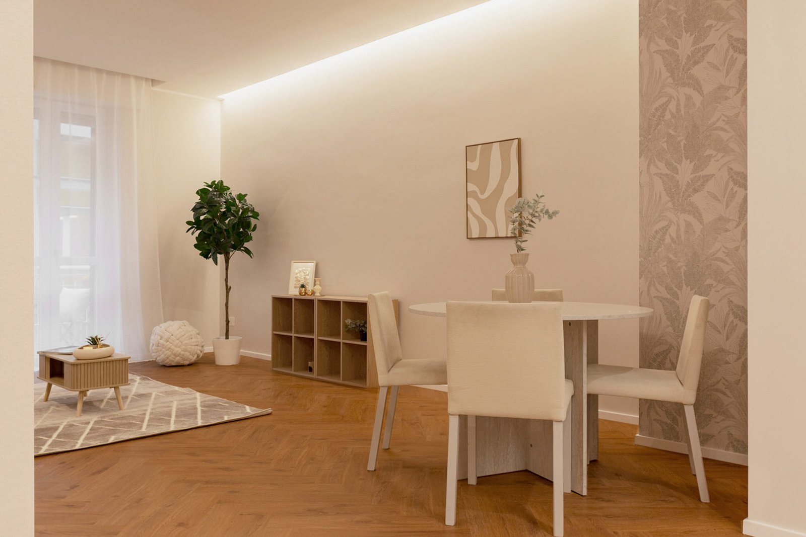 4_home-staging-soggiorno-zona-pranzo-moderno-minimalista-herringbone.jpg Soggiorno e zona pranzo moderna e minimalista con pavimento in legno a spina di pesce, tavolo rotondo con sedie chiare e vaso decorativo, parete con carta da parati botanica; illuminazione LED e luce naturale; sullo sfondo area living con divano, tappeto geometrico e pianta verde.