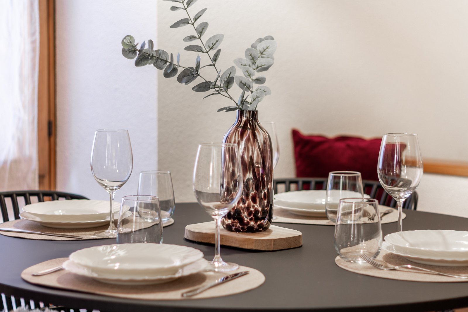 6_dettaglio-tavolo-apparecchiato-design-moderno-elegante.jpg Dettaglio di tavolo apparecchiato con piatti bianchi e calici di vetro, vaso decorativo con eucalipto su piano scuro, atmosfera elegante e curata.