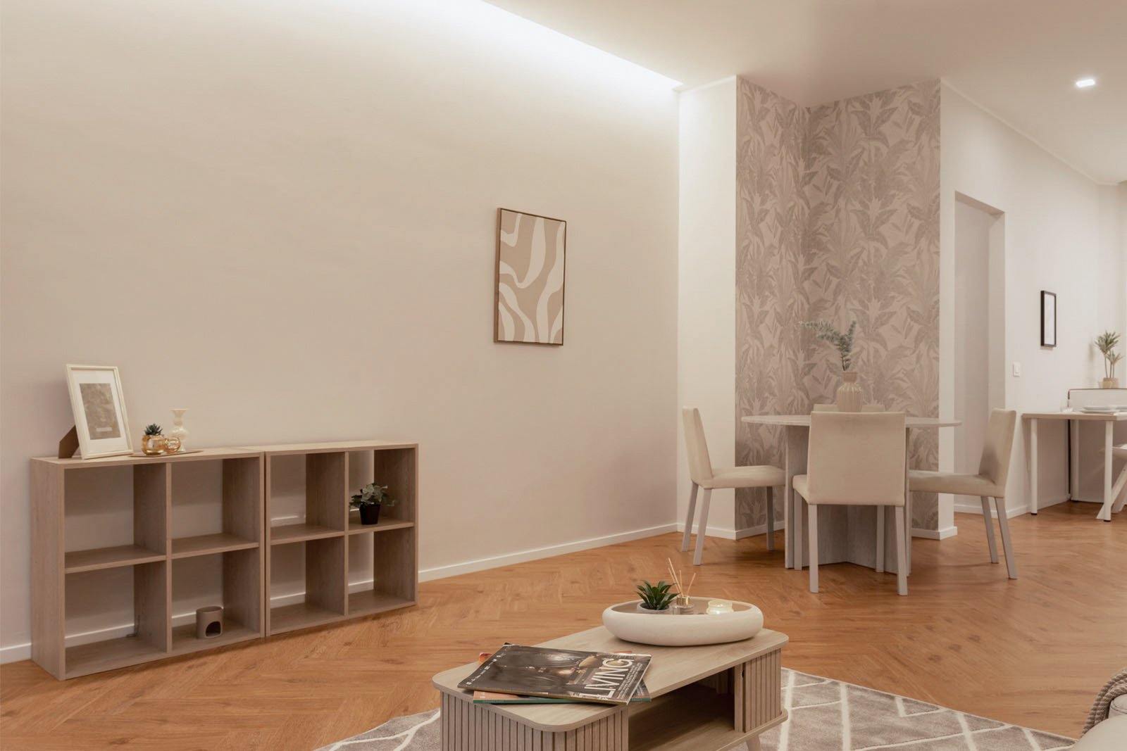 7_home-staging-soggiorno-zona-pranzo-moderno-minimalista-toni-neutri-pavimento-herringbone.jpg Soggiorno e zona pranzo moderna e minimalista con pavimento in legno a spina di pesce, tavolino con decorazioni e riviste di design, scaffale con oggetti decorativi e quadro astratto, tavolo rotondo con sedie chiare e parete con carta da parati botanica; ambiente luminoso.