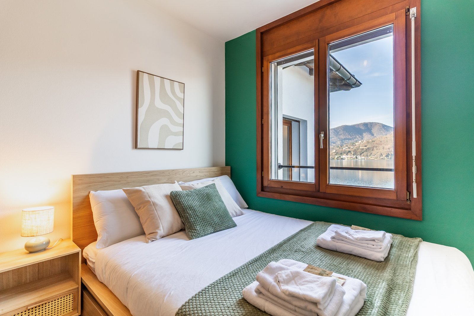 8_relooking-appartamento-camera-matrimoniale-vista-lago-parete-verde-atmosfera-calda-legno-complementi-verdi-toni-neutri.jpg Camera con vista lago e parete verde,toni neutri, arredi in legno chiaro, complementi verdi e beige; atmosfera rilassante.
