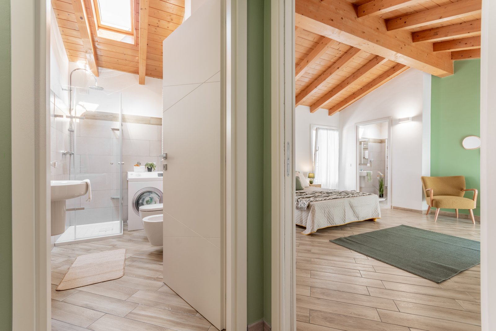 9_home-staging-collegamento-camera-bagno-mansarda-disimpegno-salvia.jpg Vista di collegamento tra camera matrimoniale e bagno mansardati, con disimpegno color salvia e ambienti luminosi con travi a vista. La camera presenta parete salvia e complementi nei toni del senape e del verde, mentre il bagno è caratterizzato da finiture tortora, doccia in vetro e sanitari bianchi.